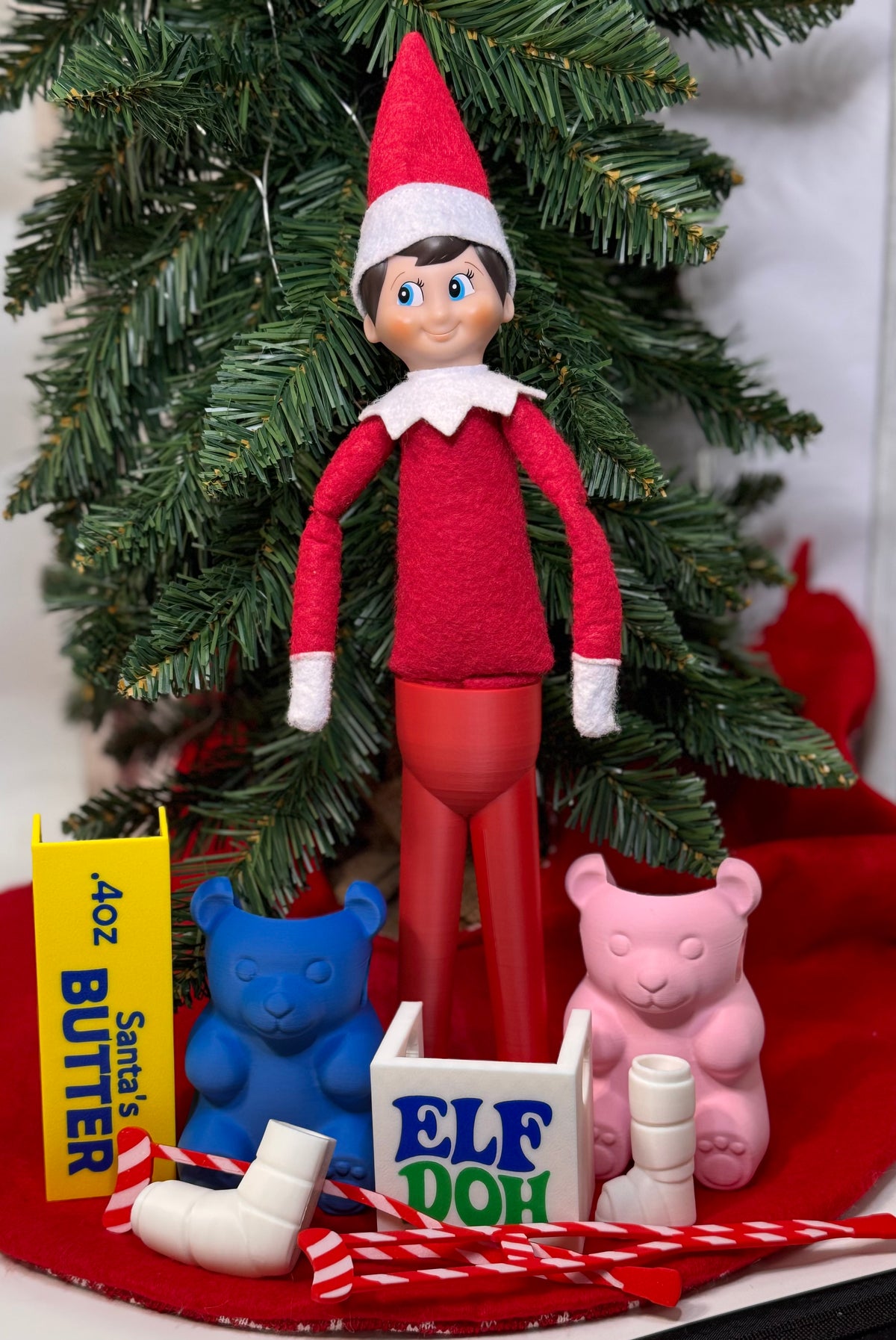 Elf doll standing upright on red 3D printed stand-up legs with white feet under a Christmas tree