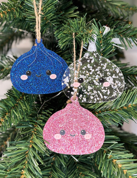 Blue, pink, and crystal flake glitter acrylic dumpling Christmas ornaments with smiling faces hanging on a Christmas tree
