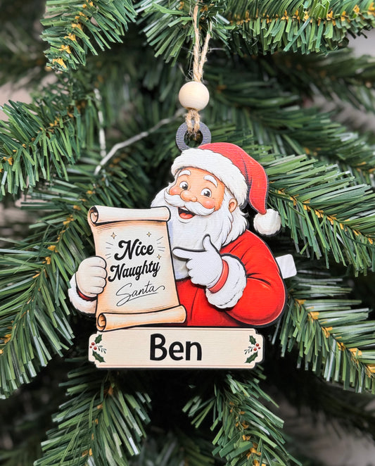Personalized naughty or nice Santa ornament with movable hand and custom name banner hanging on a Christmas tree.