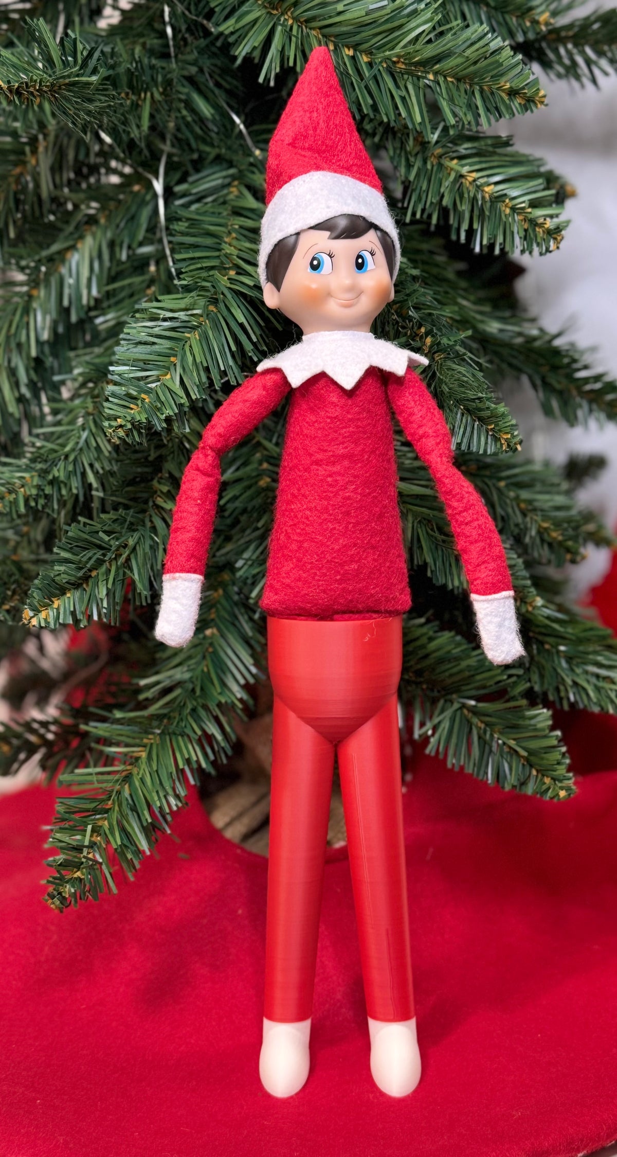 Elf doll standing upright on red 3D printed stand-up legs with white feet under a Christmas tree