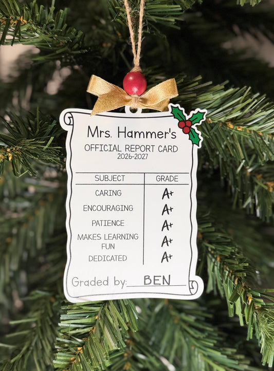Personalized teacher report card Christmas ornament with A+ grades, holly accent, and gold bow hanging on a tree.