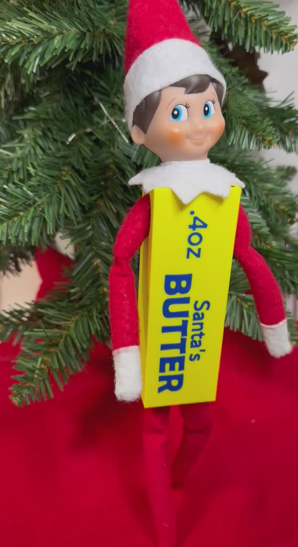 Elf doll wearing a yellow 3D printed butter stick costume with blue “Santa’s Butter” lettering, sitting under a Christmas tree